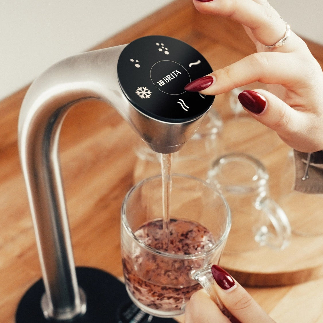 Iemand die een BRITA Extra C-Tap gebruikt om heet water in een glas met theeblaadjes te schenken.