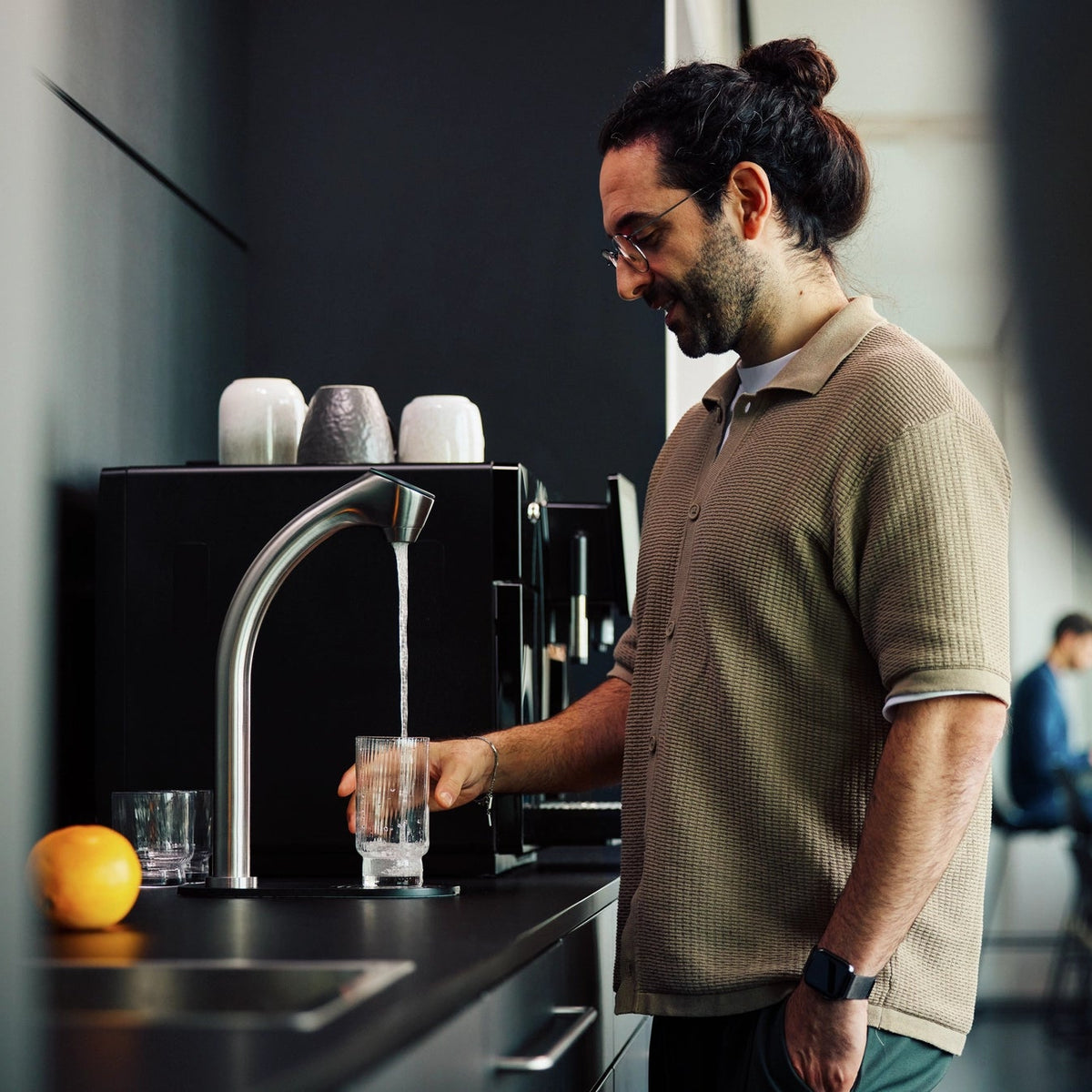 Een man in een kantoorkeuken die water uit een BRITA C-Tap in een glas schenkt.