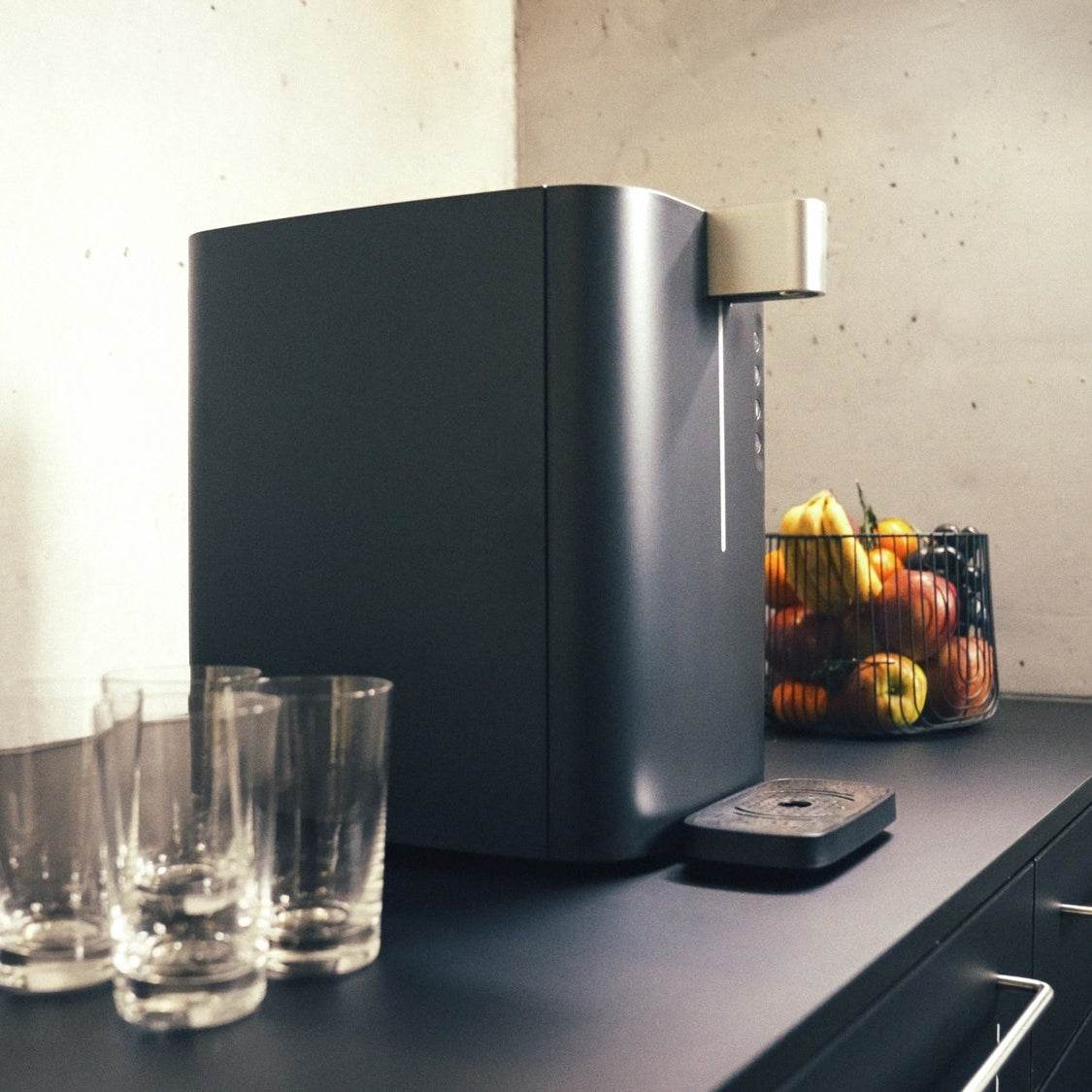 Een BRITA Top Compact op een aanrecht, met glazen en een fruitmand op de achtergrond.